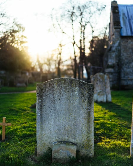 A weathered gravestone in a grassy cemetery at sunset